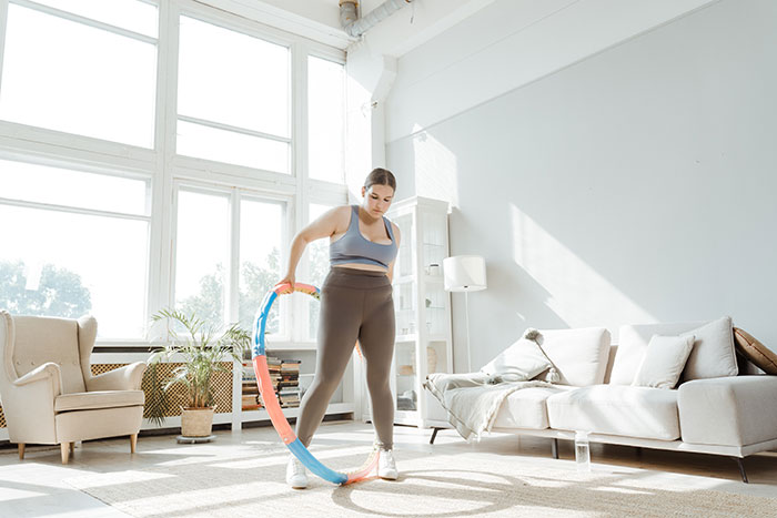 A woman trying a fun hobby with a hula hoop in her living room.