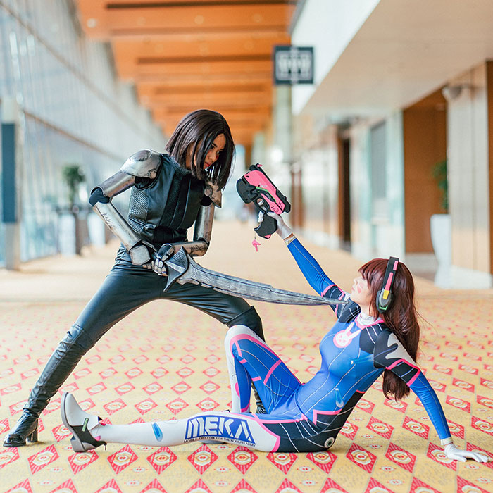 Women engaged in a cosplay duel, one pointing a sword, showcasing hobbies like cosplay events.