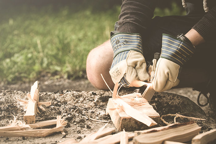 Person carving wood with gloves, showcasing creative hobbies in an outdoor setting.