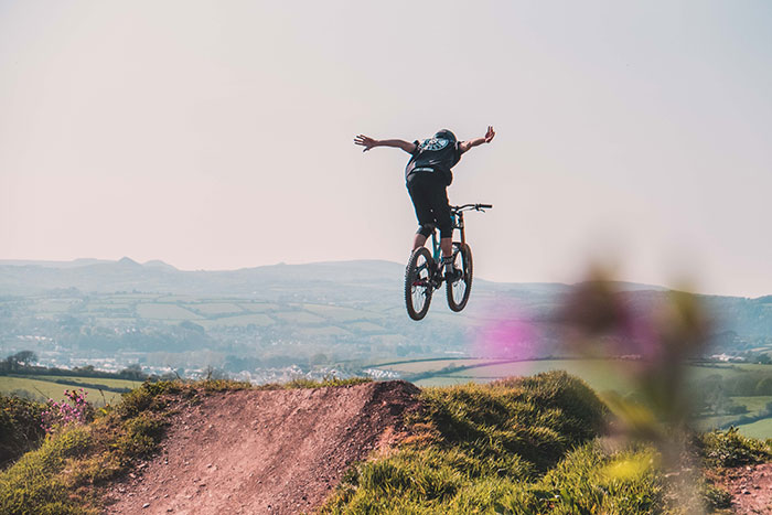 Man enjoying a fun hobby by riding a mountain bike over a scenic trail jump.