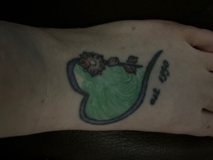 A colorful heart-shaped tattoo with flowers and the text "est 1990" on skin.