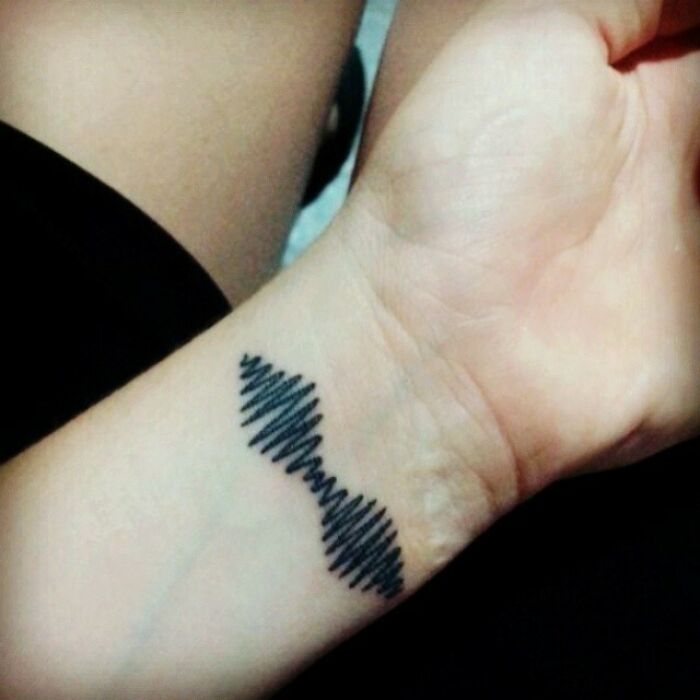 Wrist tattoo design featuring a minimalist black wave pattern.