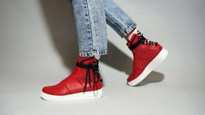 Red high-top sneakers with black laces paired with rolled-up jeans, highlighting unusual shoe style.