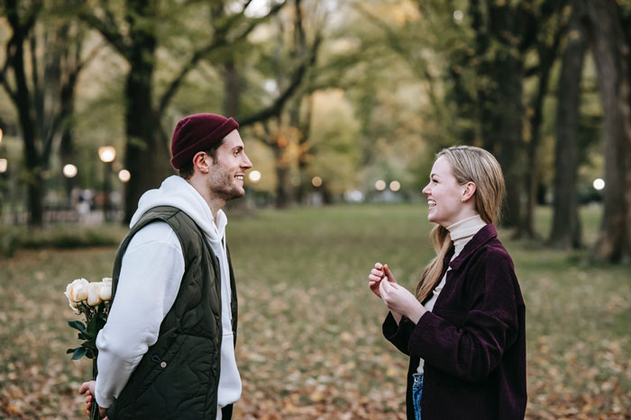 A young couple in a park exchanging millennial slang playfully, surrounded by autumn trees.