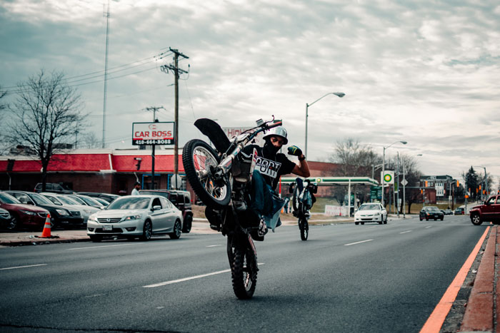 Two motorcyclists performing stunts on a city street, showcasing millennial slang culture.