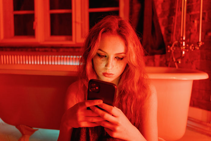 Young woman with a smartphone in a dimly lit bathroom, exploring millennial slang in a modern setting.