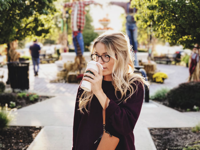 Woman sipping coffee outside, surrounded by autumn decor, reflecting millennial lifestyle.