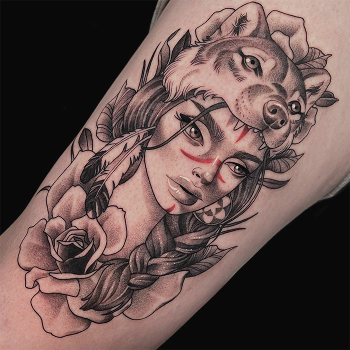 Tattoo of a woman with a wolf headdress, feathers, and roses, embodying a wild side with nature elements.