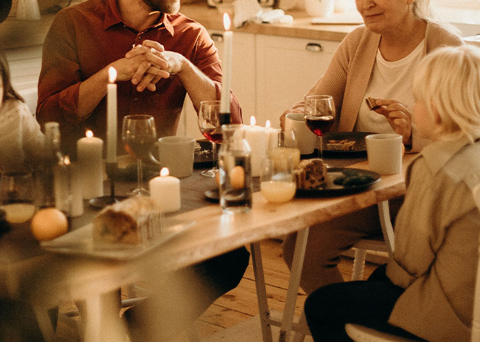 Family dinner scene with candles and food, discussing a grandmother's desire for a tattoo of her grandkid's footprint.