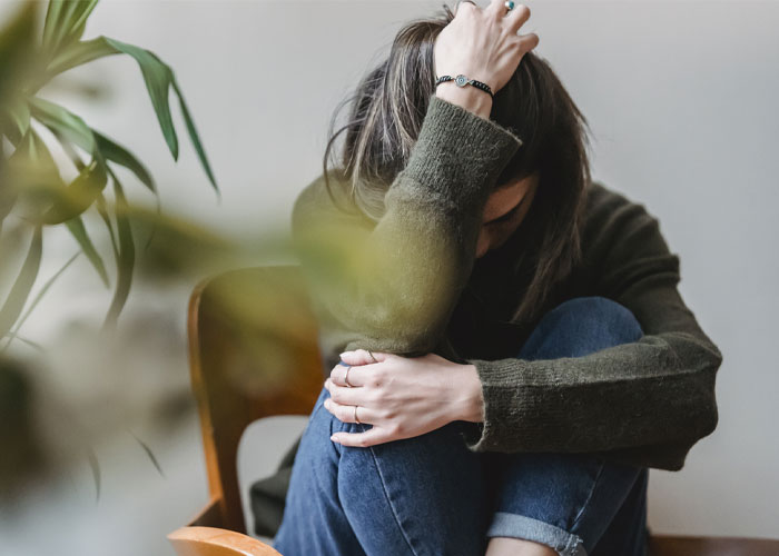 Stressed woman sitting, hand on head, contemplating issues surrounding MIL's desire for grandkid's footprint tattoo.
