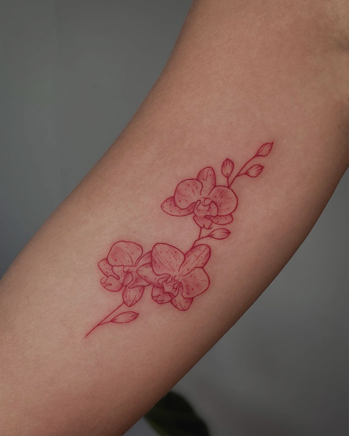 Red ink tattoo of delicate orchid flowers on forearm.