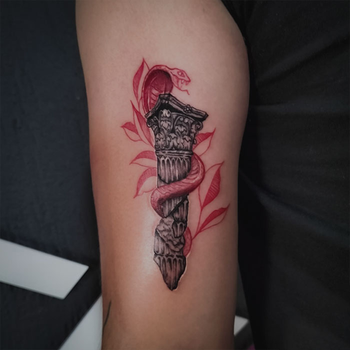 Red ink tattoo of a snake wrapped around a stone column on upper arm.