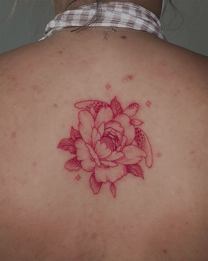 Red ink tattoo of a floral design on a person's back, featuring intricate detailing and subtle shading.