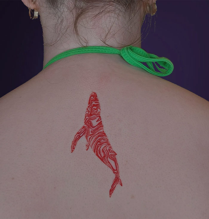 Red ink tattoo of a whale design on a person's upper back, highlighted against a green halter tie.