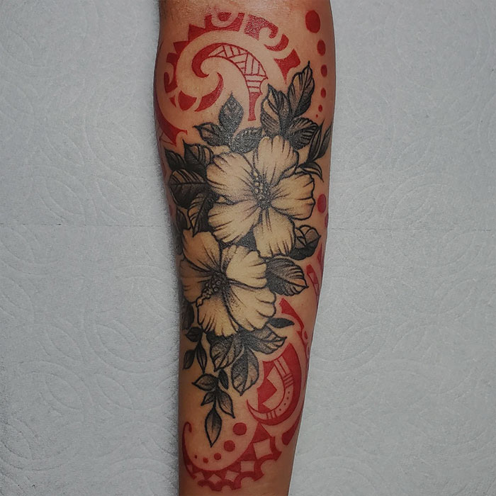 Forearm tattoo featuring black floral design with red ink accents.