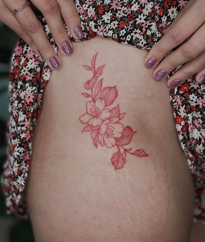 A detailed red ink flower tattoo on a person's side, showcasing intricate design elements.