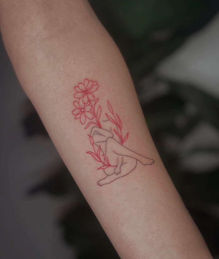 Red ink tattoo design of a minimalist figure with flowers on forearm, showcasing unique red tattoo art style.