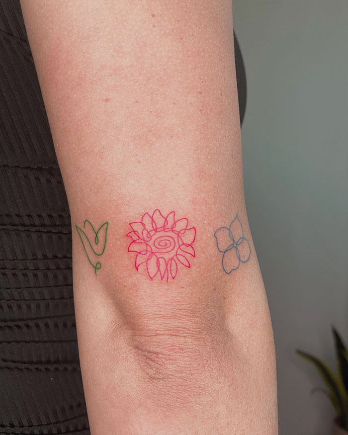 Red ink tattoo with floral design on arm, featuring minimalistic and colorful elements.