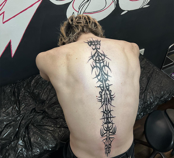 Individual showcasing an intricate spine tattoo design in a studio setting.