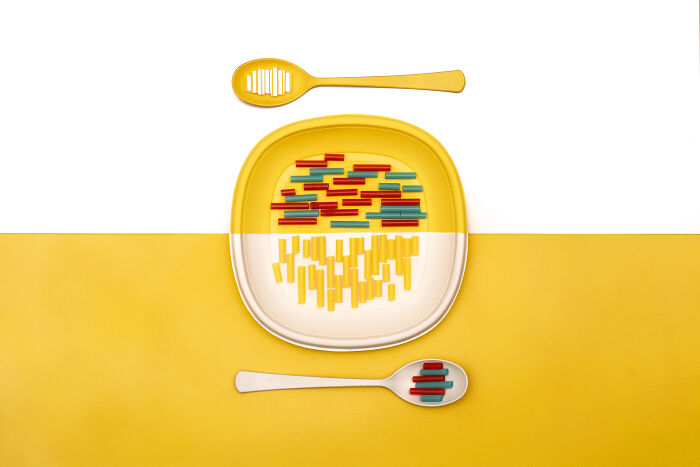 Abstract representation of global problems using colored pasta on a plate with matching spoons on a yellow and white background.