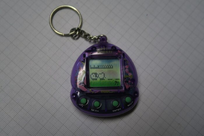 Purple digital virtual pet keychain from old gadgets that were popular trendsetters of their time displayed on graph paper background.
