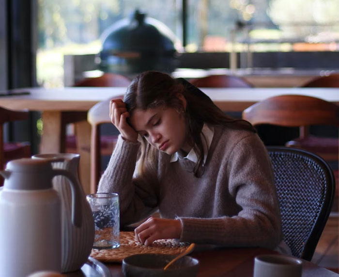 Young woman in a cozy sweater sitting at a table, appearing thoughtful while reflecting on advice from people over 50.