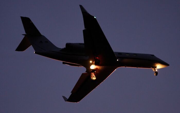 Private jet flying at dusk with illuminated landing gear, illustrating flight attendants sharing passenger annoyances online.