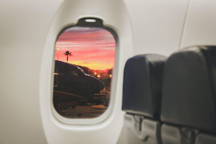View from airplane window at sunset showing another plane on the tarmac with empty flight attendant seats nearby