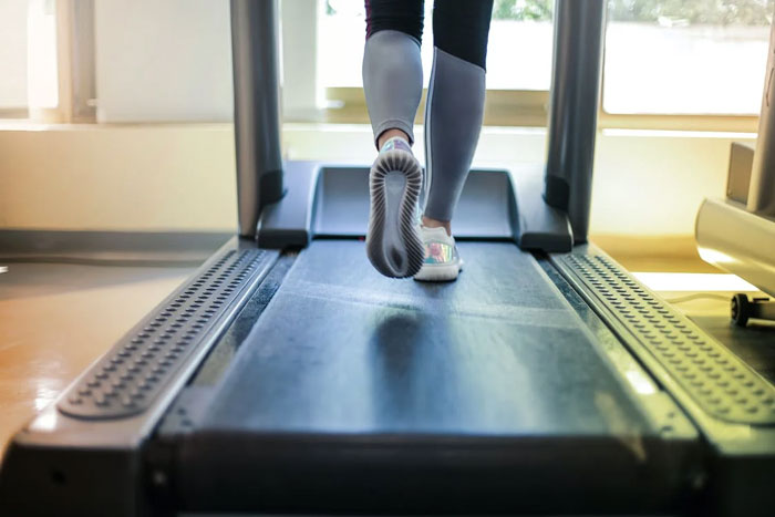 Person over 50 walking on treadmill indoors focusing on health advice shared with younger people.
