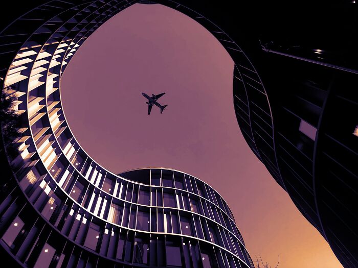 Airplane flying above modern curved buildings at sunset, illustrating flight attendants sharing passenger annoyances.