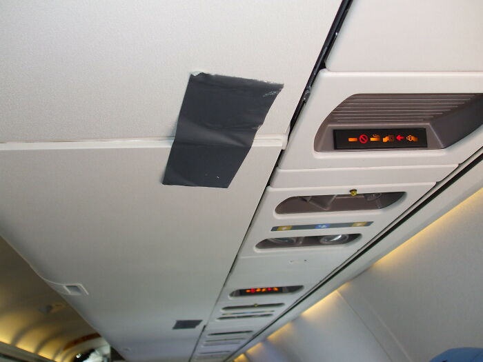 Airplane ceiling panel with duct tape near passenger service controls inside a commercial flight cabin.