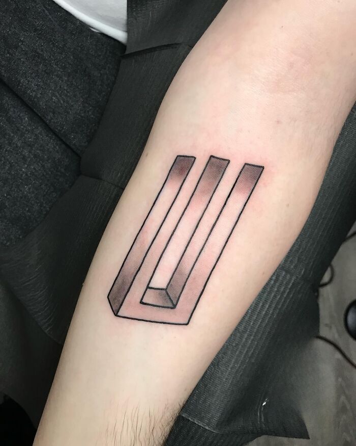 Optical illusion tattoo of a Penrose triangle on an arm, creating a 3D effect.