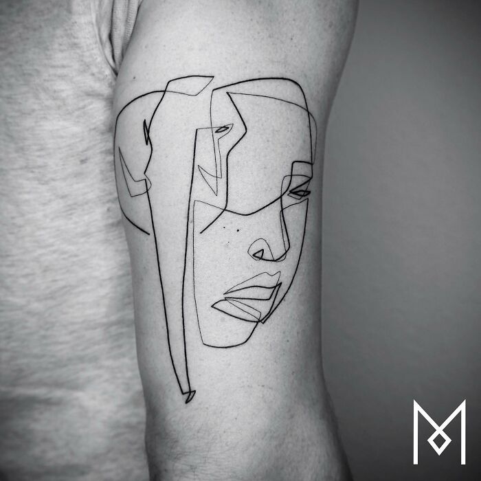 Single line tattoo on arm depicting a stylized face.