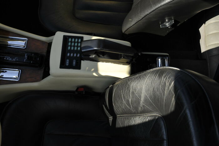 Old gadgets trendsetter vintage car phone fixed in leather car interior with control buttons on center console.