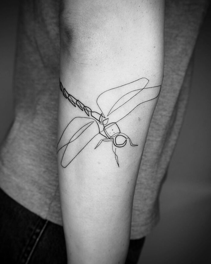 Single line tattoo of a dragonfly on an arm, showcasing minimalist artistry.