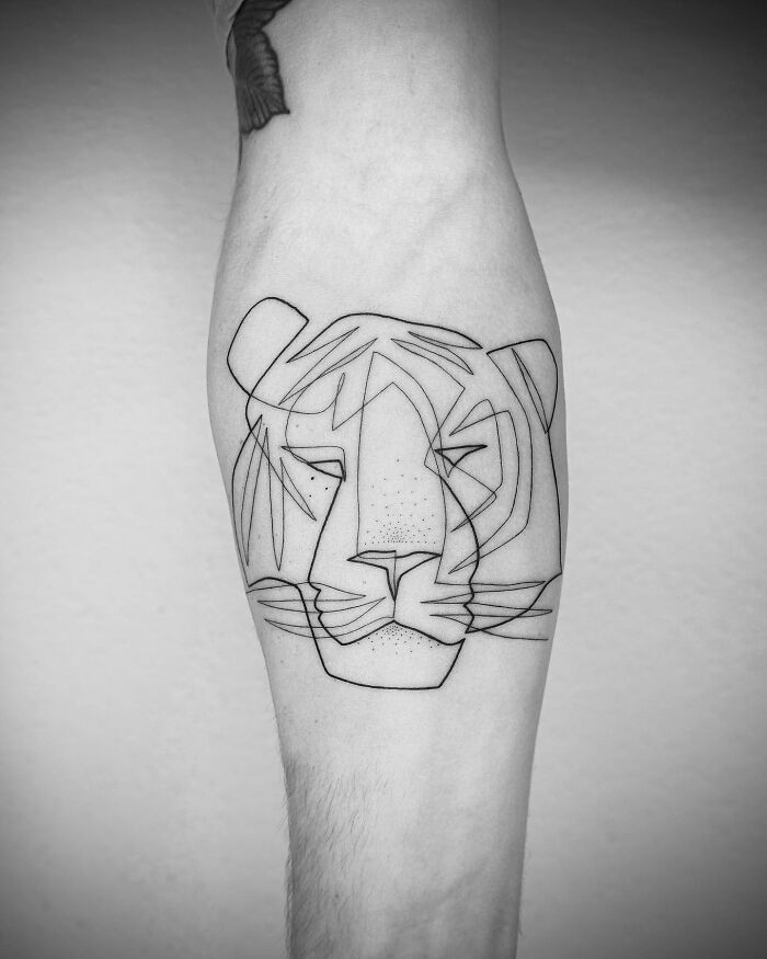 Single line tattoo of a stylized lion on inner forearm.