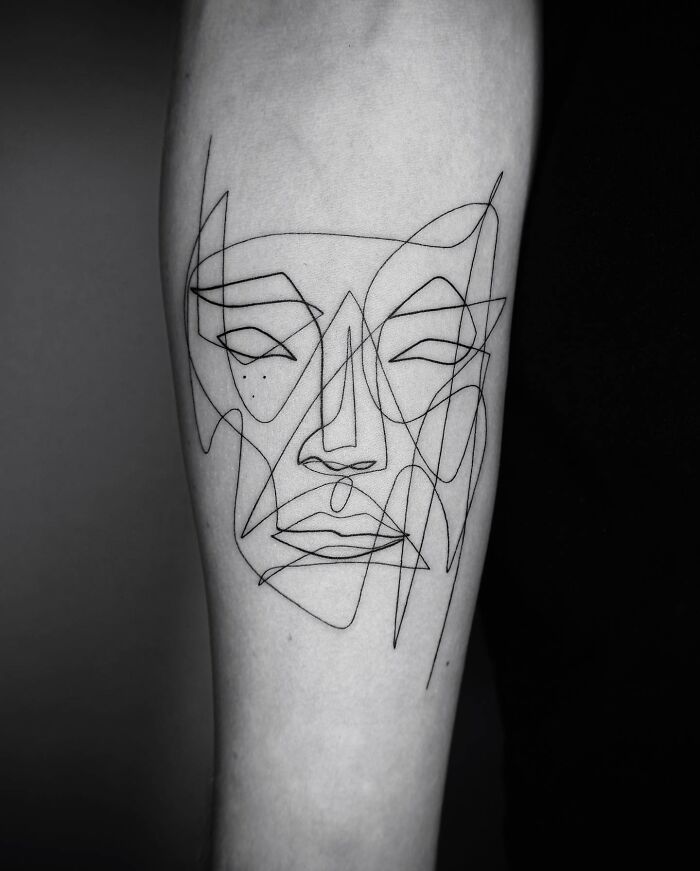 Single line tattoo art depicting an abstract face on skin.