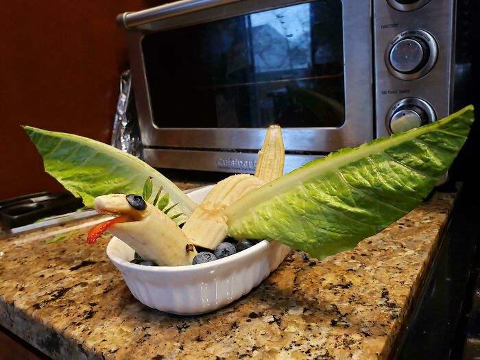 Banana and greens crafted into a bird shape, resembling unappetizing food art, placed on a kitchen counter.