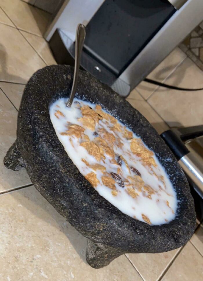 A bowl of cereal with milk served in a large stone mortar, looking unappetizing.