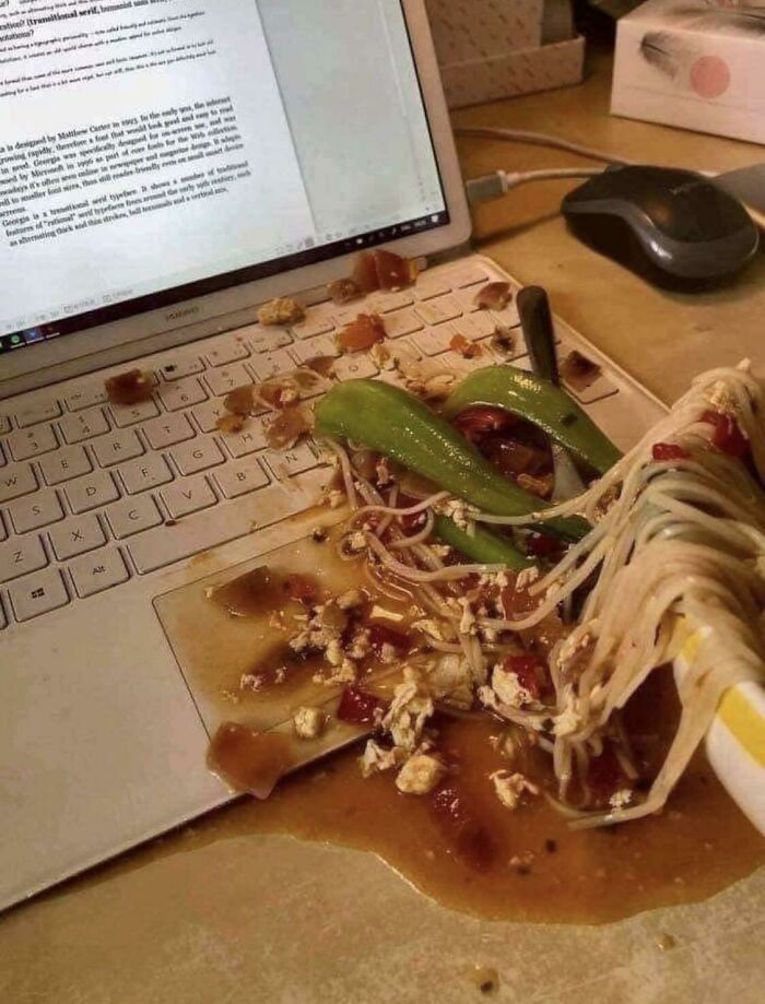 Noodles and sauce spilled on a laptop keyboard, creating a mess that looks anything but appetizing.
