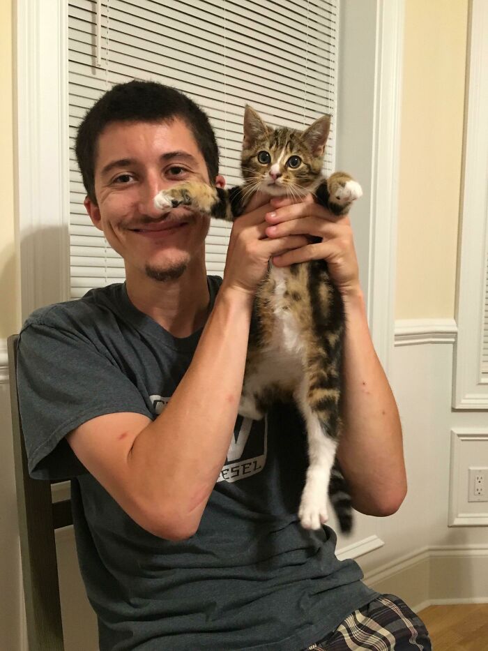 Man holding one of the cutest cats ever with a playful expression in a cozy indoor setting.