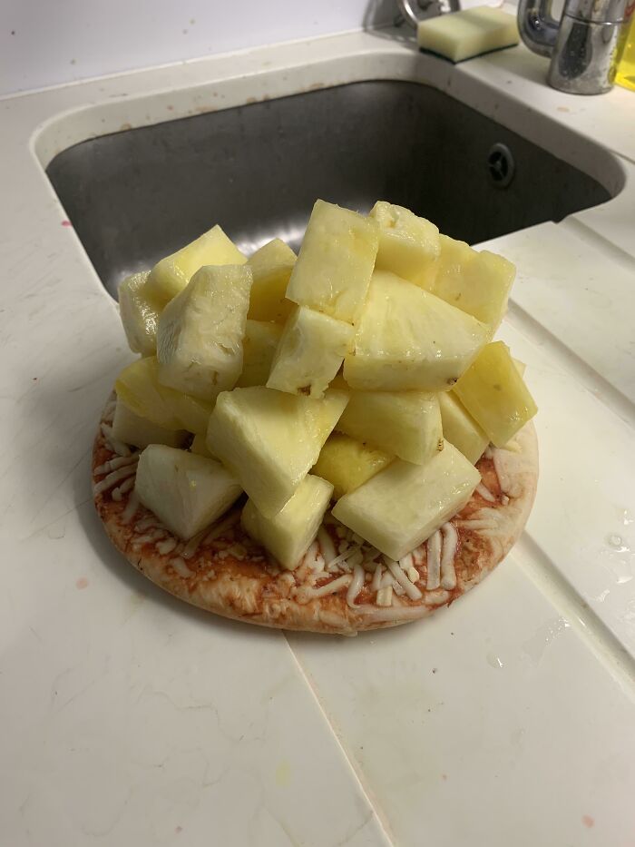 Unappetizing food pic of a pizza base piled with pineapple chunks by a sink.