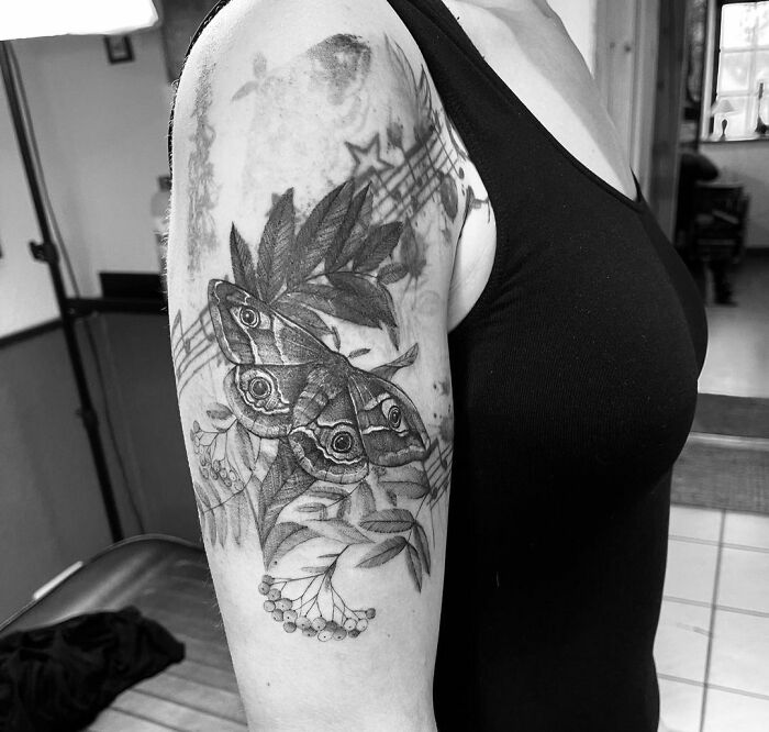 Arm with nature tattoo featuring a detailed moth and leaves, highlighting the human-earth bond in artistic design.