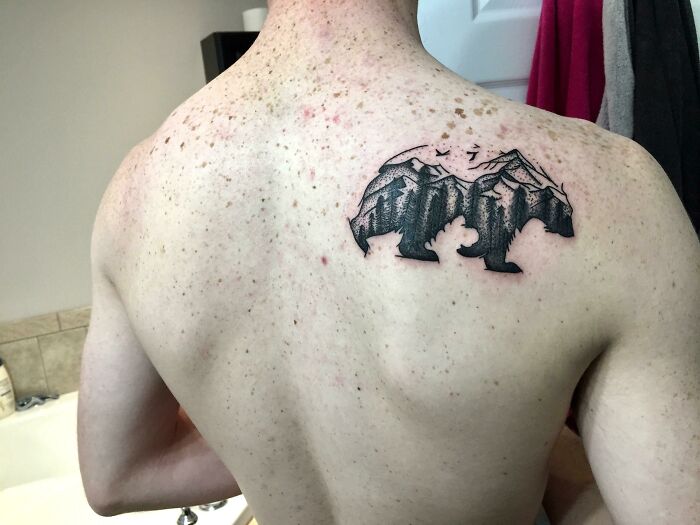 Bear-shaped nature tattoo on a man's back, symbolizing human-earth bond with mountains and trees.