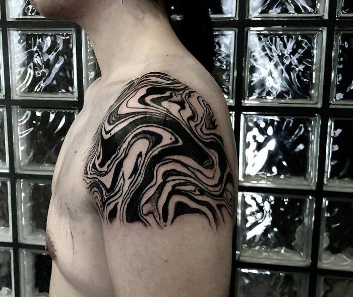 Optical illusion tattoo with mind-bending design on a person's shoulder, featuring black and white patterns.