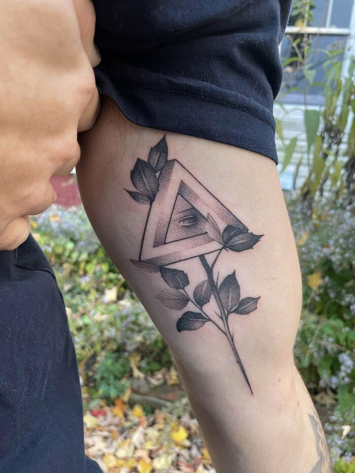 Arm with optical illusion tattoo featuring an eye within a triangle and leaves.