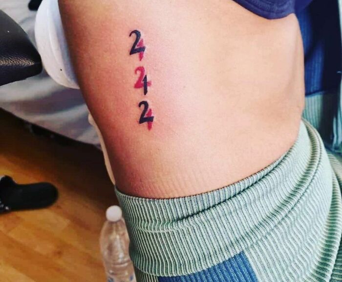 Red ink tattoo of the numbers 2, 4, and 2 on a leg, featuring bold black and red outlines.