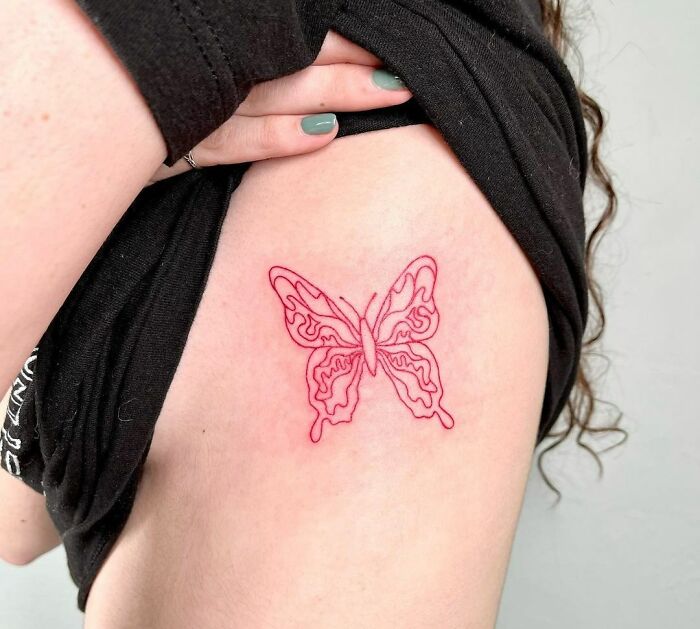 Red ink butterfly tattoo design on skin, showcasing delicate linework and vibrant color.