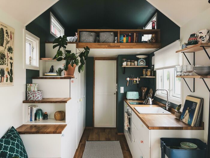 Cozy tiny house kitchen with white cabinets, wooden countertops, and green walls creating a warm and functional space.
