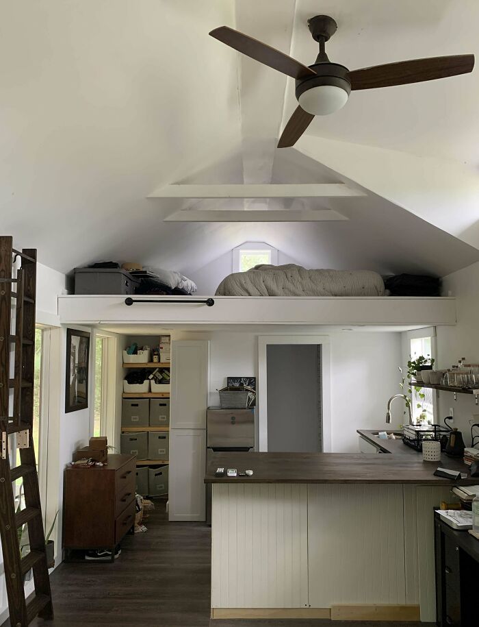 Cozy interior of a tiny house with loft bed, kitchen, and ceiling fan, showcasing smart space utilization.